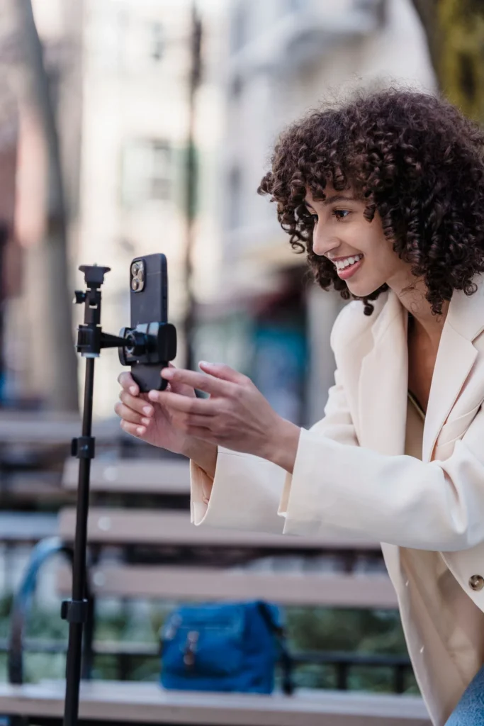 Femme souriante qui se filme avec son smartphone sur trépied pour créer ses vidéos
